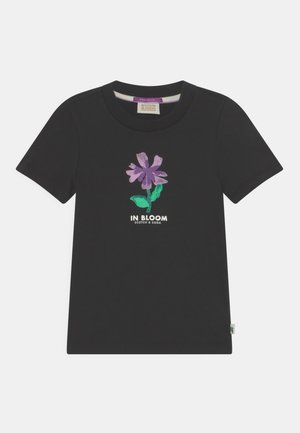 Sort t-shirt med korte ærmer med lilla blomstergrafik og grønne blade, med teksten "IN BLOOM SCOTCH & SODA" på forsiden.