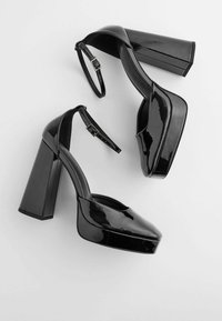 Chaussures à talons hauts en cuir verni noir avec une semelle plateforme, un talon bloc épais, une bride de cheville et un design à bout arrondi. Fini lisse et brillant.