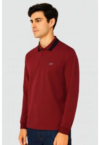Polo a maniche lunghe rosso con colletto nero, caratterizzato da un piccolo logo sul petto e una texture liscia. Design a vestibilità regolare.