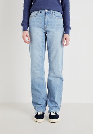 Jeans en denim bleu clair avec une coupe droite, cinq poches et une taille mi-haute. Associés à des baskets navy avec des lacets blancs.