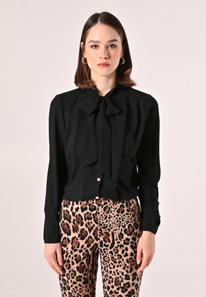 Blusa nera con colletto a fiocco e maniche lunghe, abbinata a pantaloni beige con stampa leopardata. Tessuto morbido, design aderente.