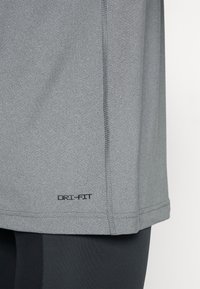 Grå DRI-FIT treningsskjorte med en glatt tekstur, med flate sømmer og en logo ved kanten. Stoffet ser lett og pustende ut.