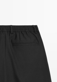 Pantalon noir avec une taille élastique, texture lisse et une poche arrière unique avec un détail de couture horizontale.