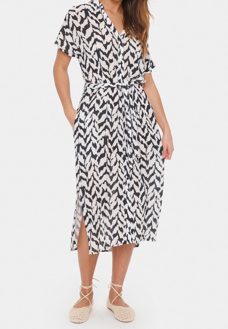Sukienka z krótkimi rękawami w czarno-białym wzorze zygzaka, zaakcentowana w talii pasującym paskiem, z bocznymi rozcięciami dla zwiększenia swobody ruchów.