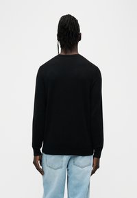 Pull noir à manches longues, col rond et poignets côtelés, associé à un jean bleu clair. Texture lisse, sans motifs ni accents visibles.