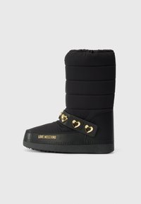 Zwarte gewatteerde enkellaars met een platte zool, voorzien van een decoratieve riem met gouden hartvormige accenten en logo details aan de zijkant.