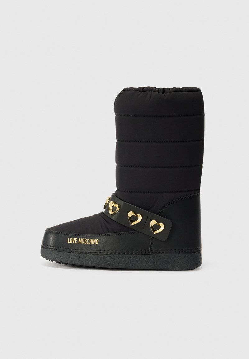 Zwarte gewatteerde enkellaars met een platte zool, voorzien van een decoratieve riem met gouden hartvormige accenten en logo details aan de zijkant.