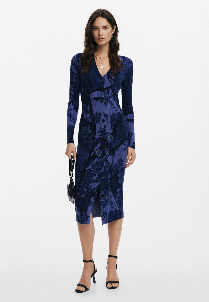 Tumedast sinise ja lillemustriga, pikkade varrukatega, pehme lõikega kleit, millel on V-dekoltee ja splitsis hem. Kandub mustade rihmaga kontsakingade ja väikese kotiga.