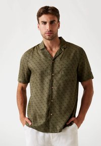 Chemise à manches courtes, vert olive, avec un motif r�épétitif vert foncé, fermeture à boutons, et une poche poitrine, fabriquée en tissu léger.