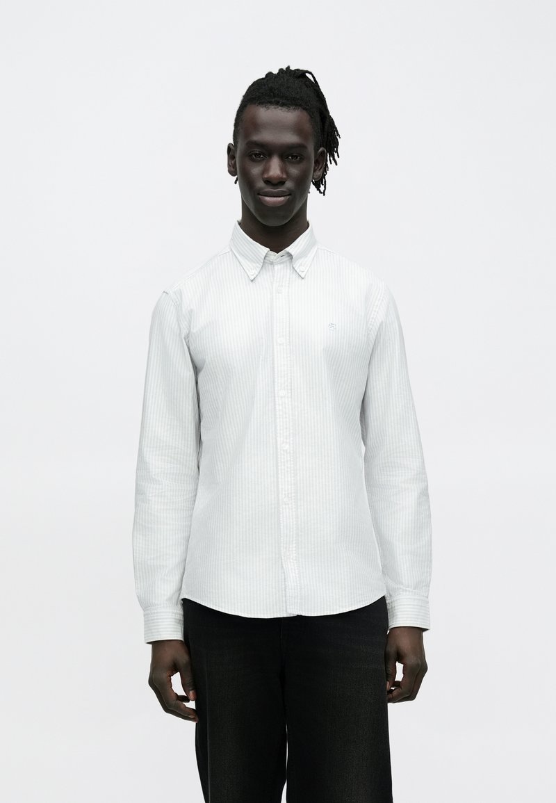 Camisa de manga larga con rayas blancas y cuello abotonado, combinada con jeans oscuros. Presenta una textura sutil y un diseño ajustado.