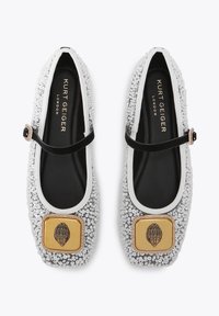 Ballerines argentées étincelantes avec des accents noirs, ornées d'une décoration carrée dorée et d'une sangle noire traversant le pied. Doublure intérieure lisse.