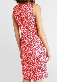 Rotes und weißes Spitzenkleid mit floralem Muster, ärmelloses Design, knielanger Schnitt und taillierte Silhouette. Strukturiertes Spitzenoverlay.