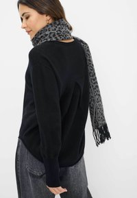 Schwarzer Pullover mit lockerer Passform, langen Ärmeln und gerippten Bündchen, kombiniert mit einem grauen Leopardenmuster-Schal mit Fransenenden.