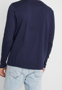 Marineblaue Langarmbluse mit Rundhalsausschnitt und glattem Stoff, kombiniert mit hellblauen Jeans aus Denim mit Gesäßtaschen und dezenten Waschdetails.