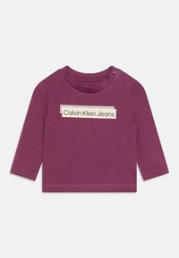 Langärmliges lila Shirt mit Rundhalsausschnitt, Druckknopf an der Schulter und rechteckigem "Calvin Klein Jeans"-Logo in Creme.
