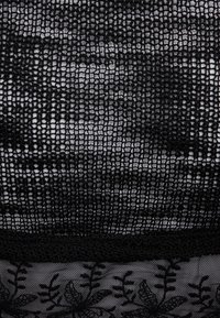 Schwarzer Spitzenstoff mit einem komplizierten offenen Muster. Der untere Abschnitt zeigt bestickte Blumenmuster vor einem transparenten Hintergrund.