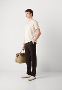 Šviesiai smėlinės spalvos trumpomis rankovėmis polo marškiniai su subtiliu raštu, derinami su juodomis kelnėmis ir baltais sportiniais batais. Laikoma šviesiai ruda savaitgalio kuprinė.