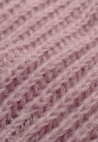 Miękka, różowa dzianina o puszystej fakturze, z wzorem wypukłych ściegów w układzie diagonlanym.