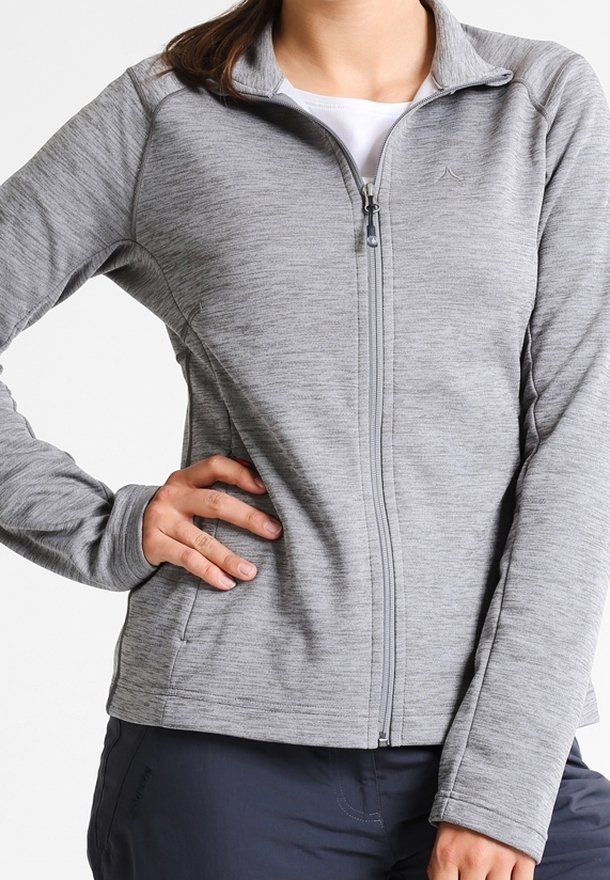 Femme portant une veste zippée intégrale gris clair avec col montant, main sur la hanche, et pantalon foncé sur fond blanc.