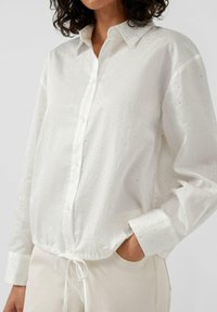 Weißes Hemd mit Button-Up-Verschluss, silbernen Punktmustern, langen Ärmeln und einem Kordelzug-Saum. Hergestellt aus leichtem Stoff mit lässiger Passform.