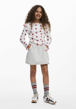 Cămașă albă cu mâneci lungi și modele cu inimioare, garnitură roșie. Fustă-pantalon cu dungi, accente roșii. Șosete gri cu dungi roșii, adidași argintii.