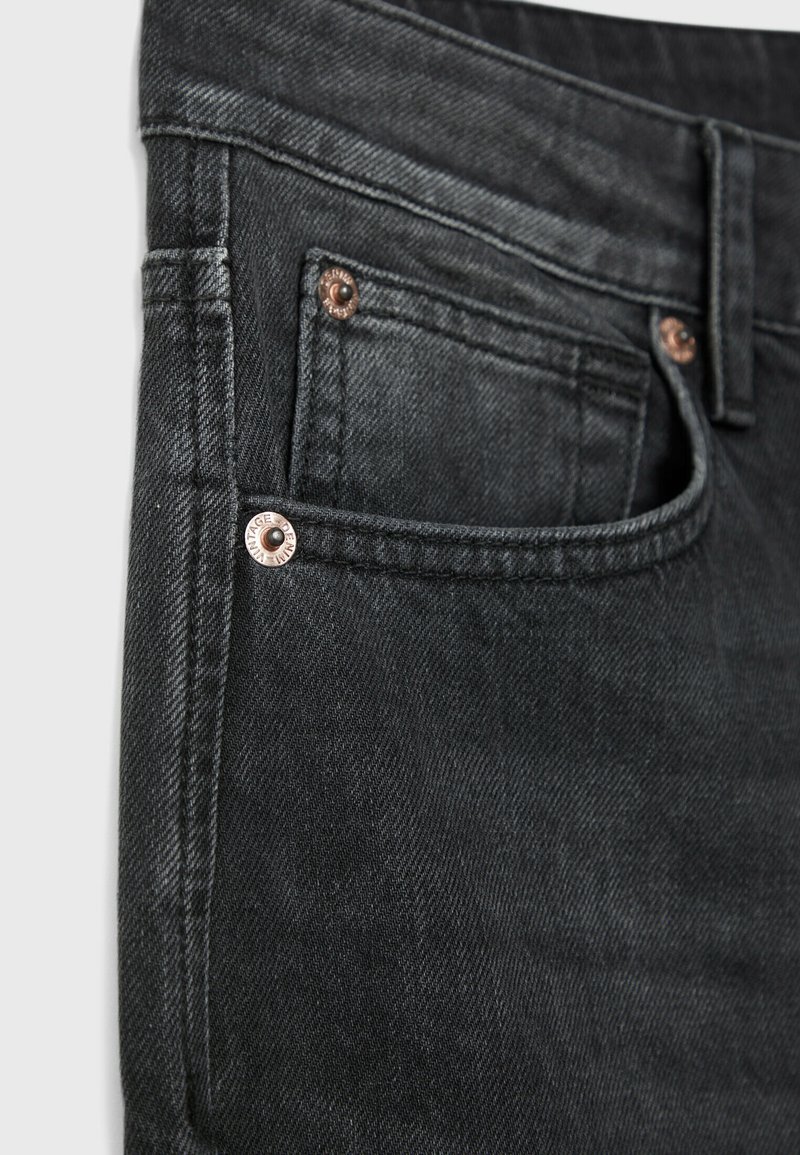 Primo piano di una tasca di jeans neri in denim con cuciture visibili e rivetti di rame sui bordi della tasca.