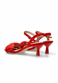 Sandalias de tacón alto rojas con detalle de lazo anudado, parte trasera abierta y correas en los tobillos. Presentan un acabado brillante y una forma de tacón acampanado.