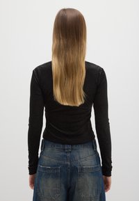 Schwarzes Langarmshirt mit strukturiertem, geripptem Design, kombiniert mit hoch taillierter blauer Jeanshose, die zwei Gesäßtaschen und ein verwaschenes Finish aufweist.