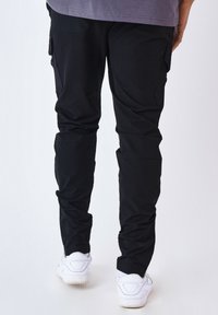 Pantalones cargo negros con un corte ajustado, hechos de material ligero. Presentan bolsillos laterales y detalles cosidos. Combinados con zapatillas blancas.
