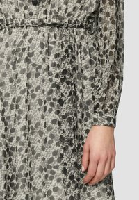 Robe transparente avec un motif à taches noir et gris, dotée d'une taille froncée et de détails à boutons sur le devant. Manches longues et fluides.