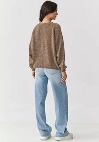 Brązowy sweter dzianinowy o luźnym kroju, w połączeniu z jasnoniebieskimi dżinsami; ma szerokie rękawy i ściągacze, oferując miękką teksturę.