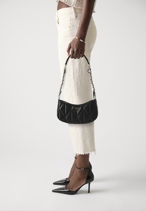 Personne portant un jean court écru et des talons hauts noirs, tenant un petit sac à main noir matelassé avec bandoulière chaîne.