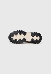Suola di sneaker nera e beige con un design robusto caratterizzato da profonde scanalature e una superficie testurizzata per garantire aderenza.