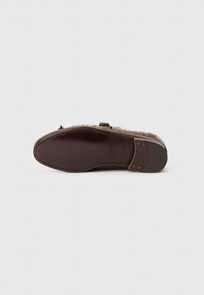 Brown leather shoe with a soft, fuzzy interior. Features a smooth sole and simple hardware detail on the side. Flat design with a rounded toe.