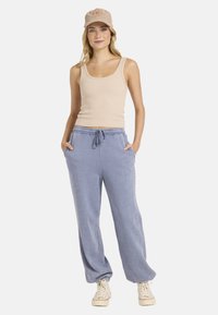 Jasbeżowy prążkowany top na ramiączkach oraz miękkie niebieskie dresy z elastycznym pasem, bocznymi kieszeniami i luźnym krojem. Beżowa czapka z detalem logo.