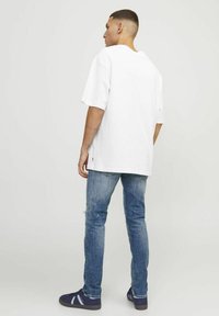 Camiseta blanca de gran tamaño con mangas cortas, combinada con unos vaqueros desgastados azules y zapatillas navy con acentos blancos. Estilo y diseño casual.