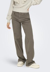 Pantalones de pierna ancha de talle alto en verde oliva oscuro, fabricados en algodón, con cinco bolsillos y una textura suave, combinados con zapatillas de color claro.