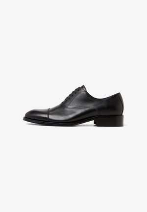 Black leather dress shoe with a smooth finish, round toe, and textured panel on the upper, featuring five eyelets and a low heel.
