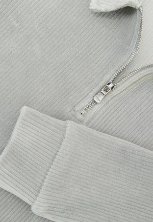 Lysegrå sweatshirt i ribbet stof med en sølvfarvet lynlås og blød tekstur. Ærmekanterne er tykke og supplerer det overordnede design.