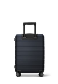 Valise rigide bleu marine avec des rainures verticales, une poignée noire rétractable et quatre roulettes noires ultra-compatibles.