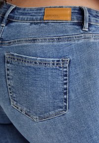 Dark blue denim jeans with a rear pocket, a brown leather tag on the waistband, and visible stitching details.