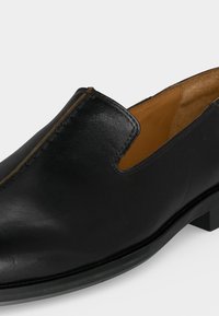 Μαύρο δερμάτινο παπούτσι τύπου slip-on με στρογγυλεμένη μύτη, χαμηλό τακούνι και ταμπά εσωτερική επένδυση.
