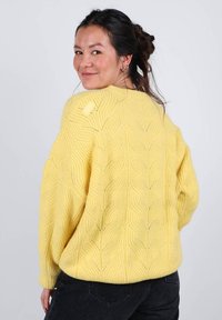 Pull jaune en tricot avec un motif texturé en forme de feuille, coupe oversize et ourlet côtelé. Le design présente un bouton au niveau du col.