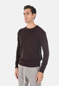 Maglione a coste marrone scuro con scollatura rotonda e maniche lunghe, abbinato a pantaloni grigio chiaro con lacci bianchi.
