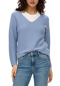 Lichtblauwe trui met een V-hals en lange mouwen, gemaakt van gestructureerde stof, gecombineerd met lichtblauwe jeans. De outfit heeft een ontspannen pasvorm.