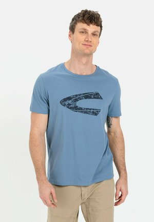 Kortærmet blå T-shirt lavet af bomuld; har et stort sort grafisk logo på forsiden. Enkelt design, simpel halsudskæring.