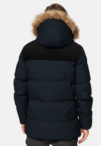 Mørkeblå pufjakke med hætte foret med kunstpels, sorte corduroy skulderdetaljer og quiltet struktur. Har en afslappet pasform og lange ærmer.