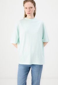 Svetle máty zelené oversized tričko vyrobené z měkké bavlny, s krátkými rukávy, vysokým kulatým výstřihem a jemnou texturou. V kombinaci s džínami.