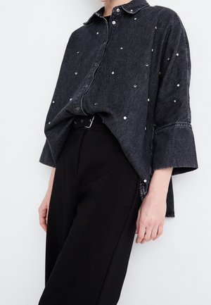 Czarna, oversize koszula jeansowa z srebrnymi ćwiekami, zestawiona z czarnymi, wysokim stanem spodniami i czarnym paskiem z srebrną klamrą.