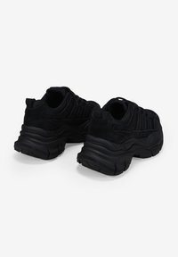 Zapatillas deportivas negras con parte superior texturizada, suela gruesa y diseño redondeado. Cuenta con un collar acolchado y una suela de goma para mayor agarre.